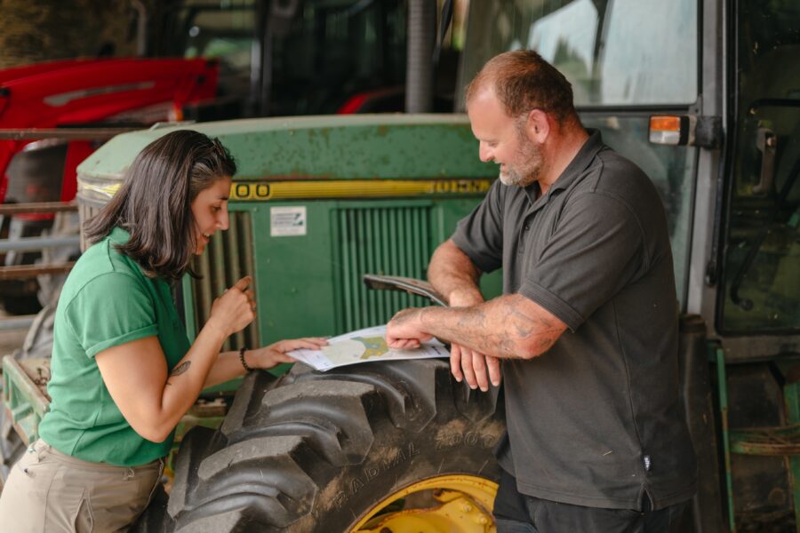 Farmer and advisor lean on tractor and study land maps